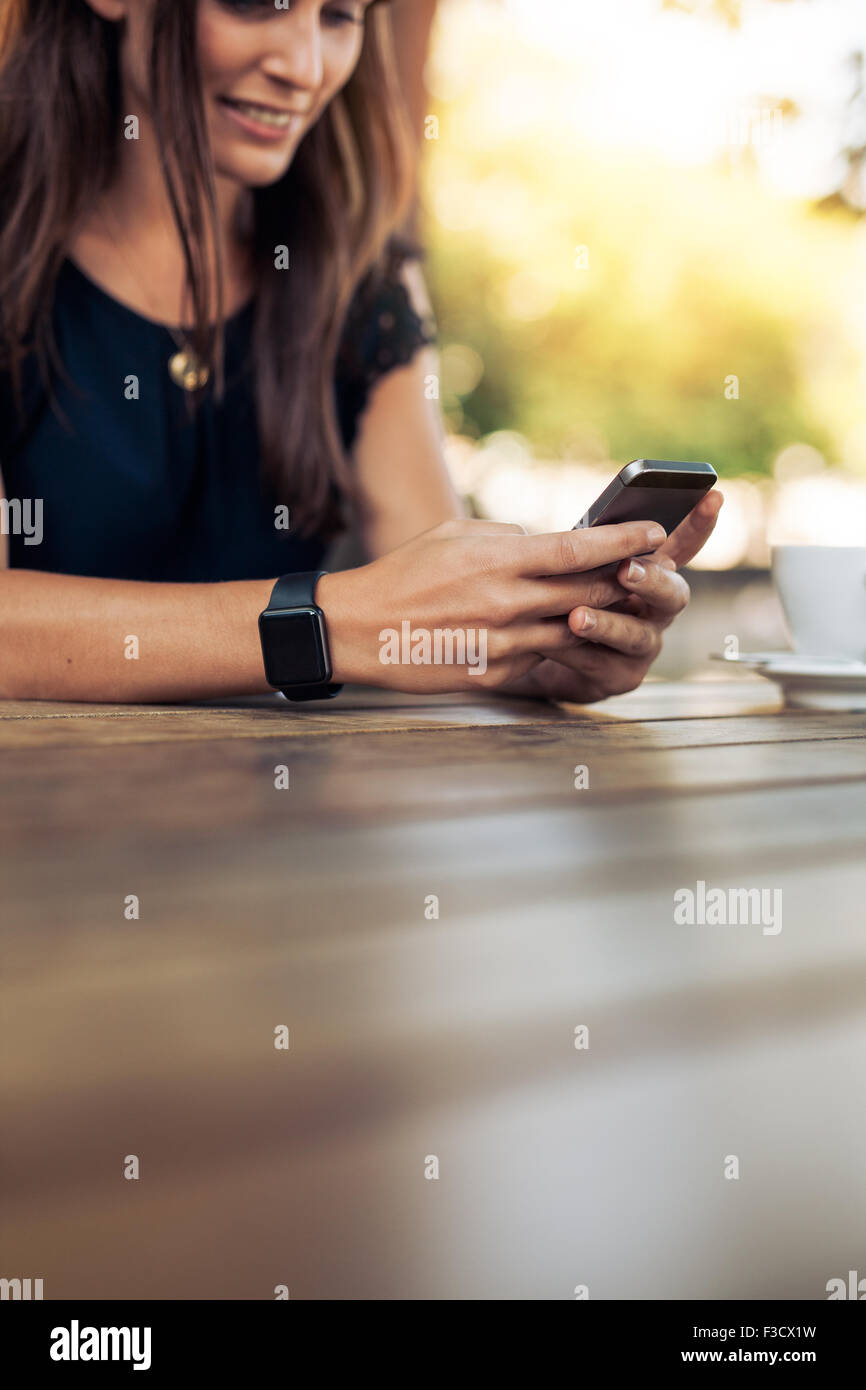 Immagine ritagliata della giovane donna utilizzando smart phone in un outdoor cafe. Femmina di lettura di un messaggio di testo sul suo telefono cellulare. Foto Stock