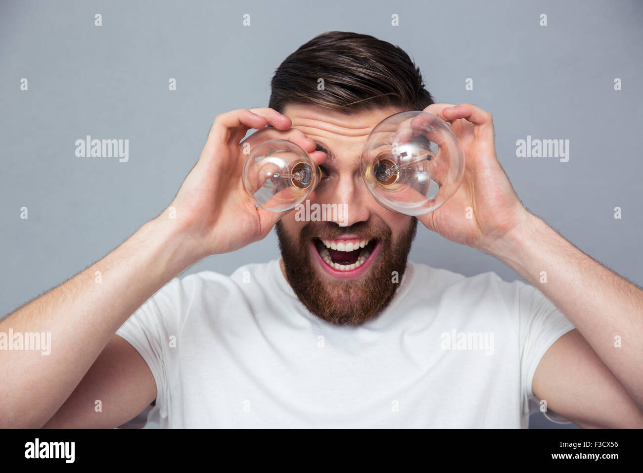 Ritratto di un uomo divertente guardando telecamera attraverso la lampadina su sfondo grigio Foto Stock