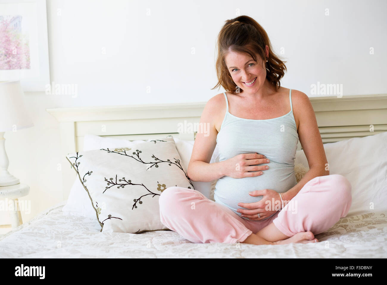 Sorridente donna incinta seduta sul letto Foto Stock