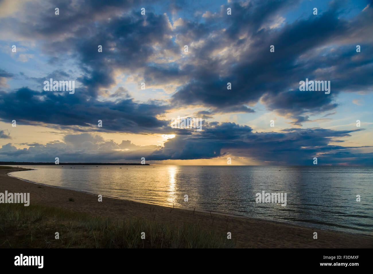 I raggi del tramonto attraverso la drammatica nuvole sopra la calma del mare e della spiaggia Foto Stock