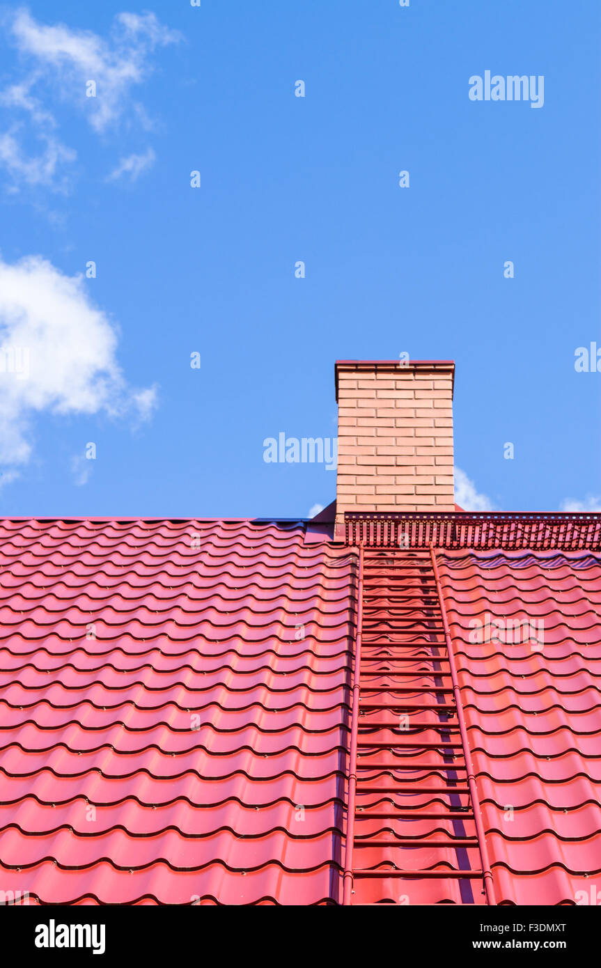 Ciminiera in mattoni sul tetto rosso con la scala di metallo contro il cielo blu Foto Stock