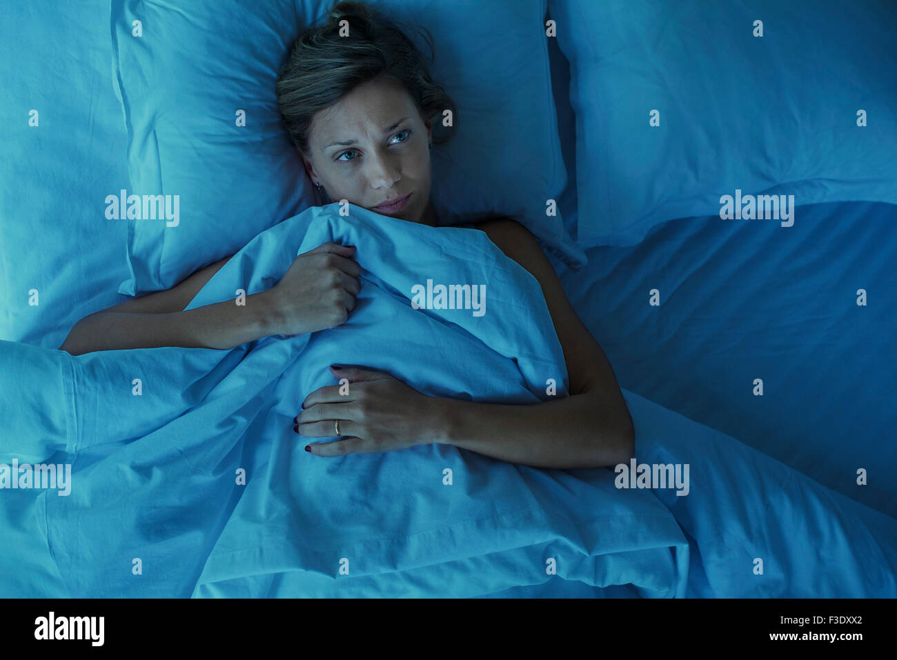 La donna che giace da sola nel letto con espressione preoccupata sul viso Foto Stock