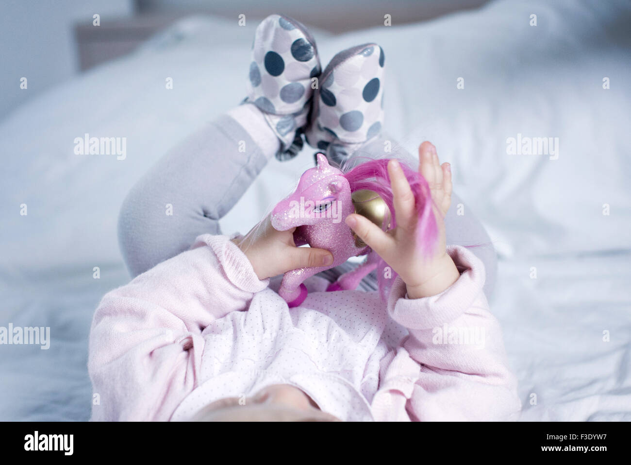 Baby girl giacente sul letto, giocando con pony giocattolo Foto Stock