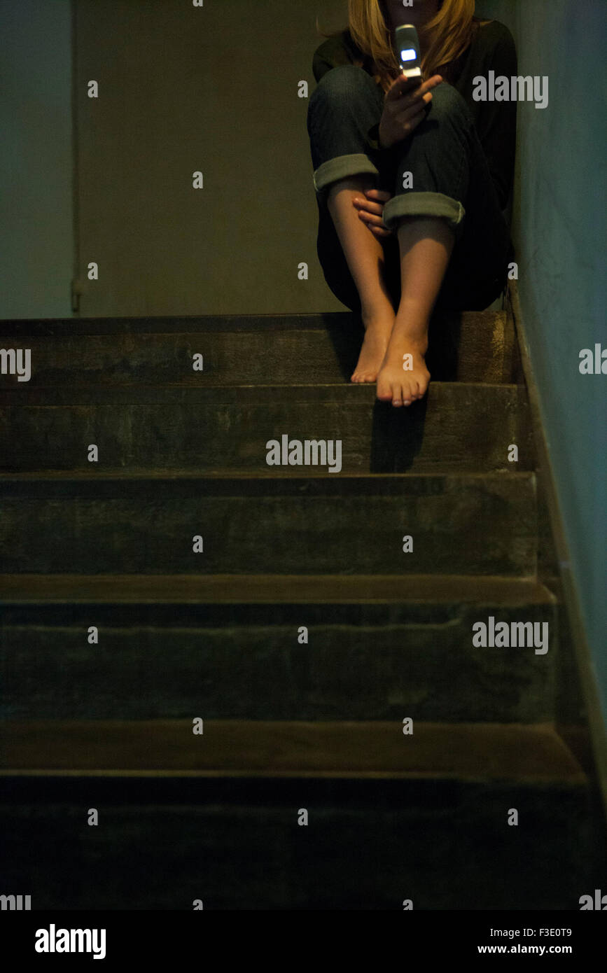 Donna seduta da sola nella tromba delle scale della messaggistica di testo Foto Stock