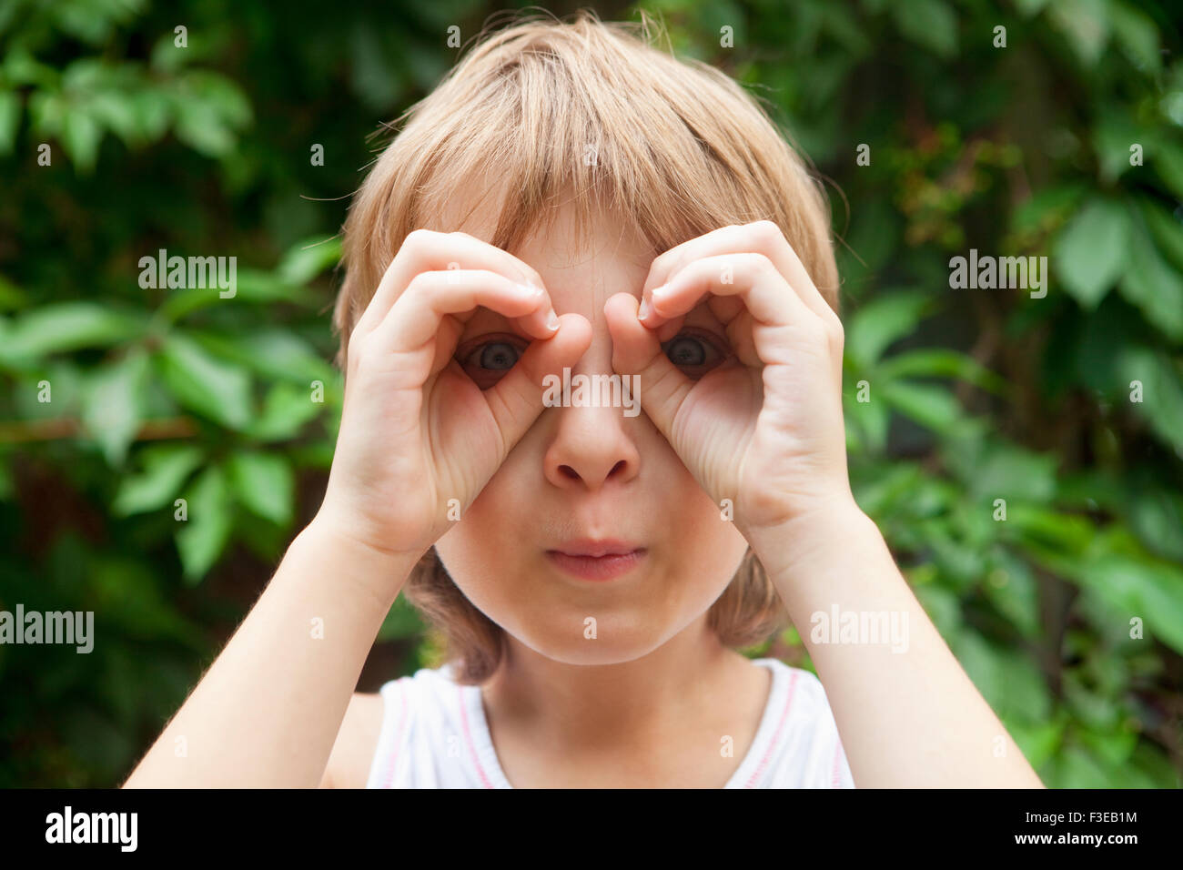 Ragazzo che guarda attraverso le dita come binocolo all'aperto Foto Stock