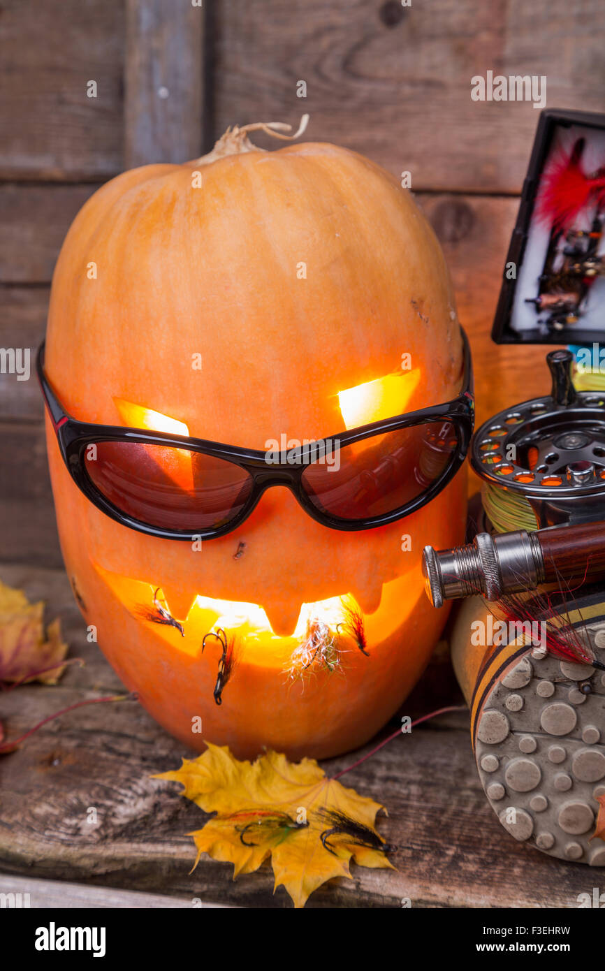 Zucca di Halloween di testa con wading boots e pesca a mosca affronta su assi di legno sfondo Foto Stock
