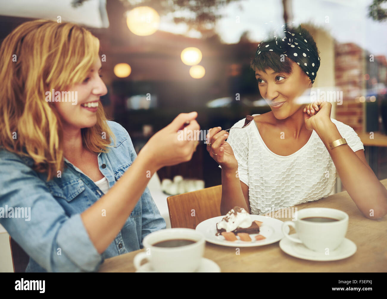 Due carismatici multi etnico ragazza giovani amici seduti a un contatore in un bar gustando una tazza di caffè mentre ridono e chat Foto Stock