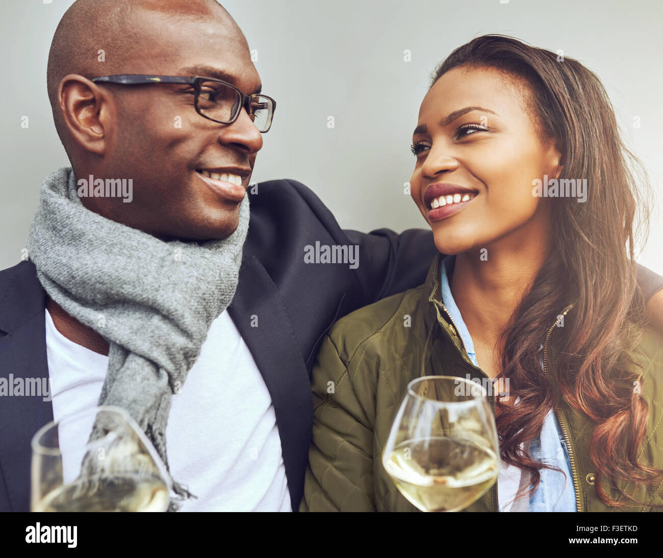 Romantico giovane americano africano giovane seduto a braccetto godendo di bicchieri di vino bianco e sorridente con amore in ogni altri e Foto Stock