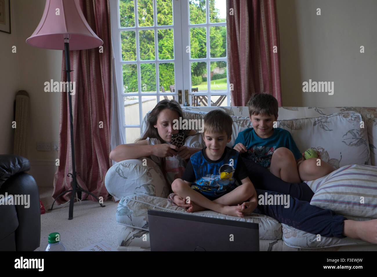 La famiglia tramite telefono cellulare e guardare i giochi per computer sul computer portatile in salotto, Stoke on Trent, Regno Unito Foto Stock