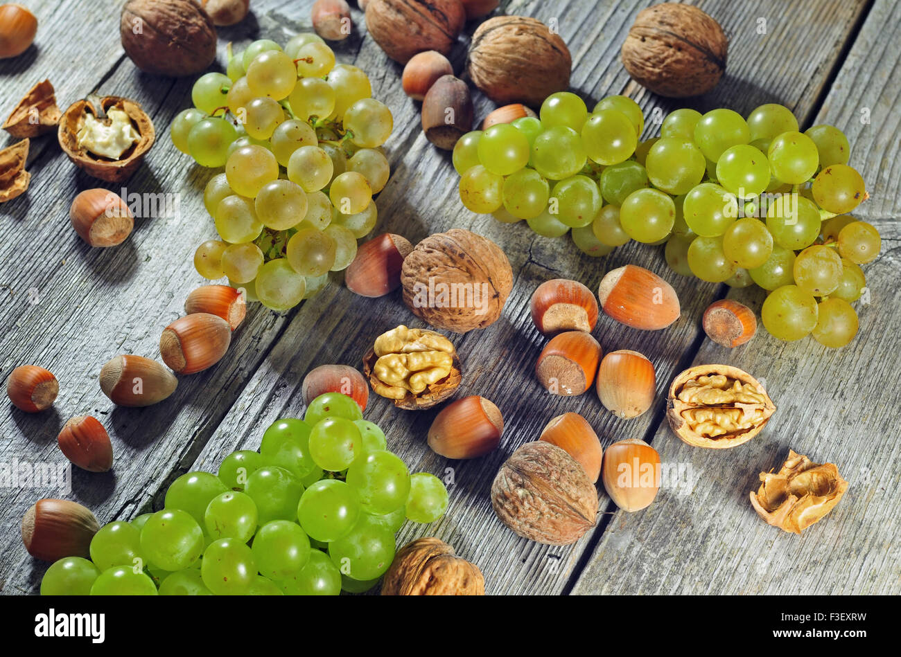 Foto di acini di uva e le nocciole nonché le noci comuni su un tavolo di legno Foto Stock