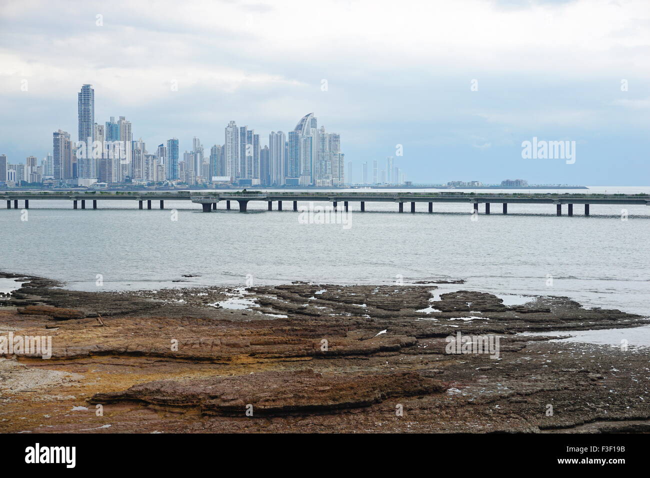 Spiaggia rocciosa in primo piano con la nuova autostrada oltre oceano e grattacieli del centro business della città di Panama, America Centrale Foto Stock