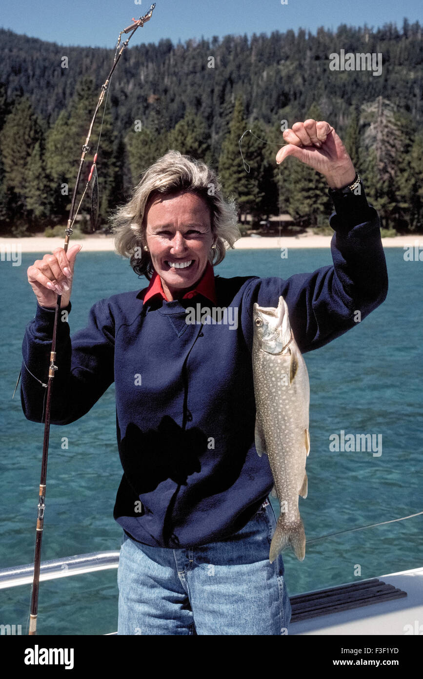 Una giovane donna mostra con orgoglio la trota di lago (Salvelinus namaycush) lei catturati durante la pesca in lago Tahoe, America del nord del più grande lago alpino. Esso si trova nelle montagne della Sierra Nevada, lungo il confine della California e Nevada, USA. Il lago di acqua dolce è anche il secondo più profonda della nazione (dopo il cratere del lago in Oregon) e la casa di altri popolare gioco di pesci tra cui il Salmone Kokanee il salmone, la trota iridea e la trota marrone. Mackinaw è il nome locale per la trota di lago. Modello rilasciato. Foto Stock