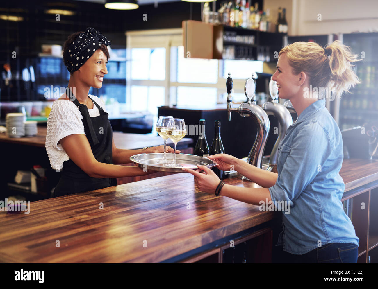 Sorridente cameriera dando bicchieri di vini su un vassoio ad una femmina di cliente al banco bar. Foto Stock