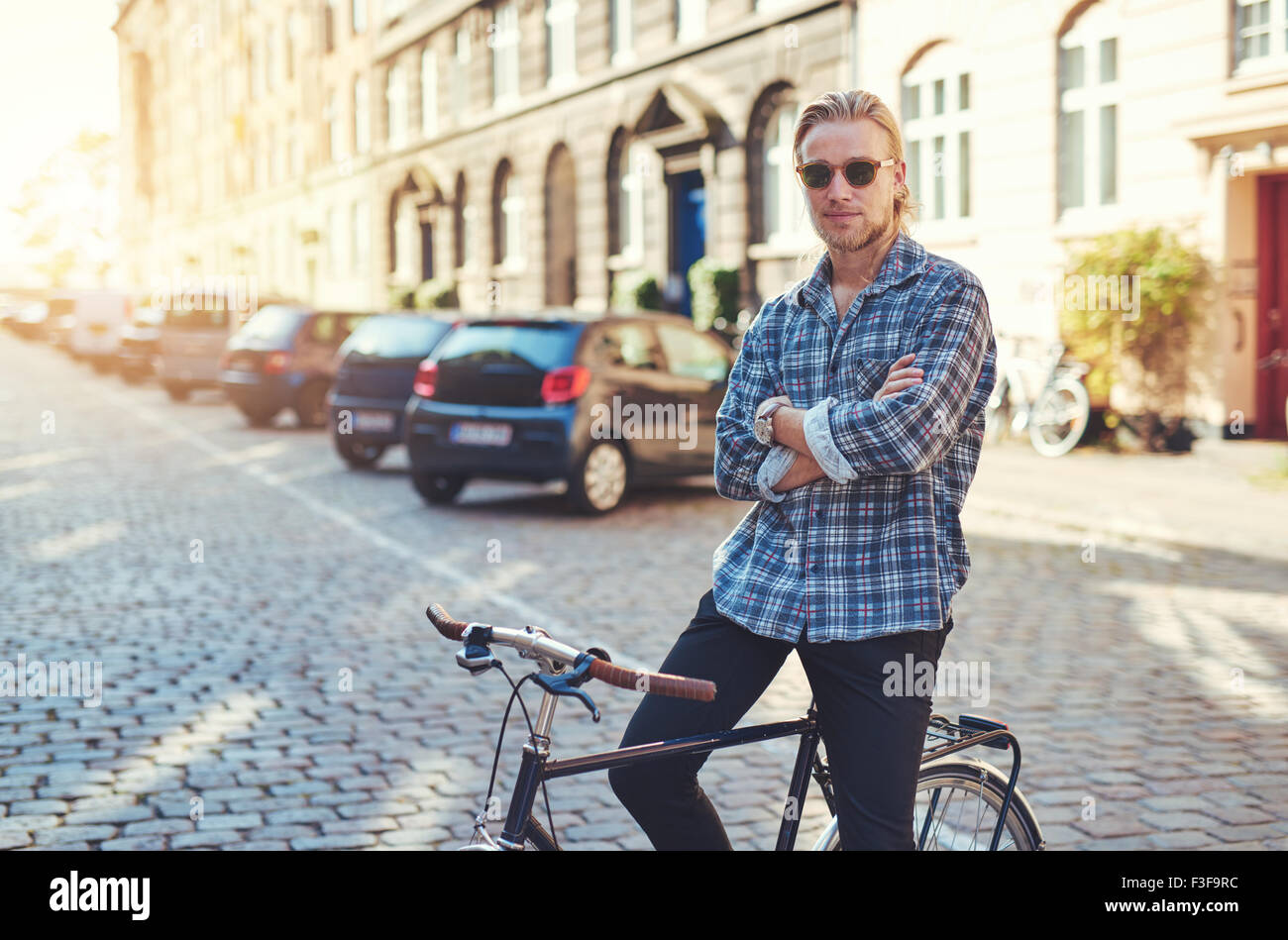Ritratto di uomo sulla sua bicicletta con le braccia incrociate cercando di stile. Lo stile di vita della città Foto Stock