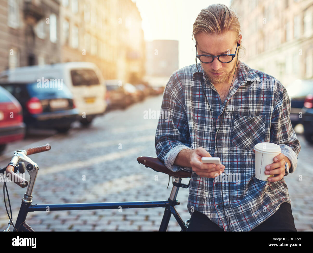 Outdoor ritratto della moderna giovane con telefono cellulare in strada, seduto sulla bici Foto Stock