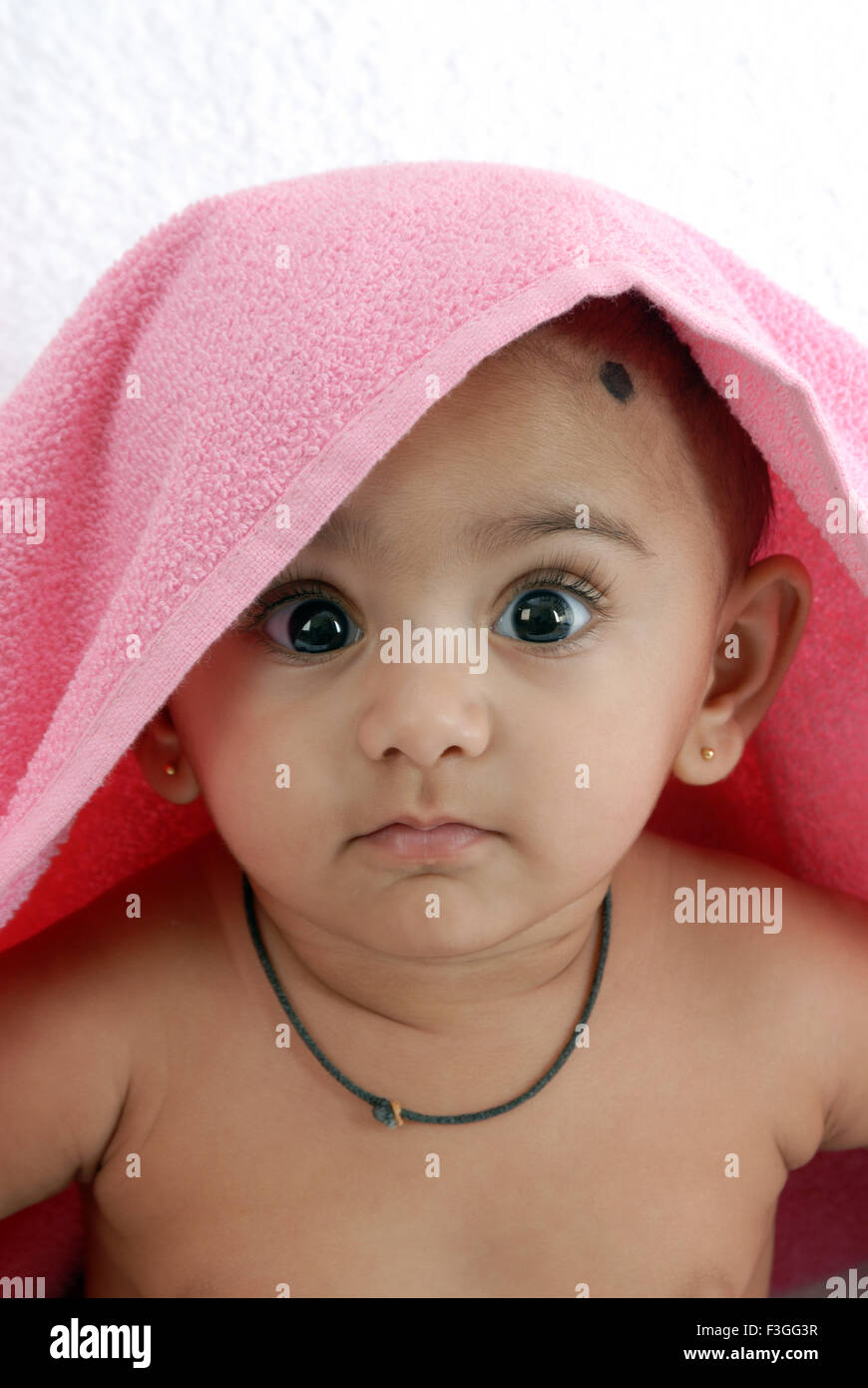 Baby boy amuleto intorno al collo e la testa coperta con asciugamani rosa guardando la telecamera signor#152 Foto Stock