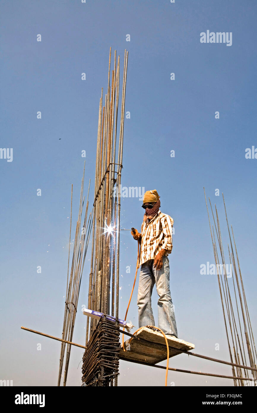 Un saldatore precariamente permanente senza un casco o una cintura di sicurezza di un sito in costruzione ; Ahmedabad ; Gujarat ; India Foto Stock