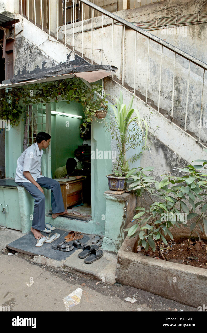 Una riparazione proprietario del negozio si trova un comodo spazio sotto le scale di un edificio ; Mumbai Bombay ; Maharashtra ; India Foto Stock