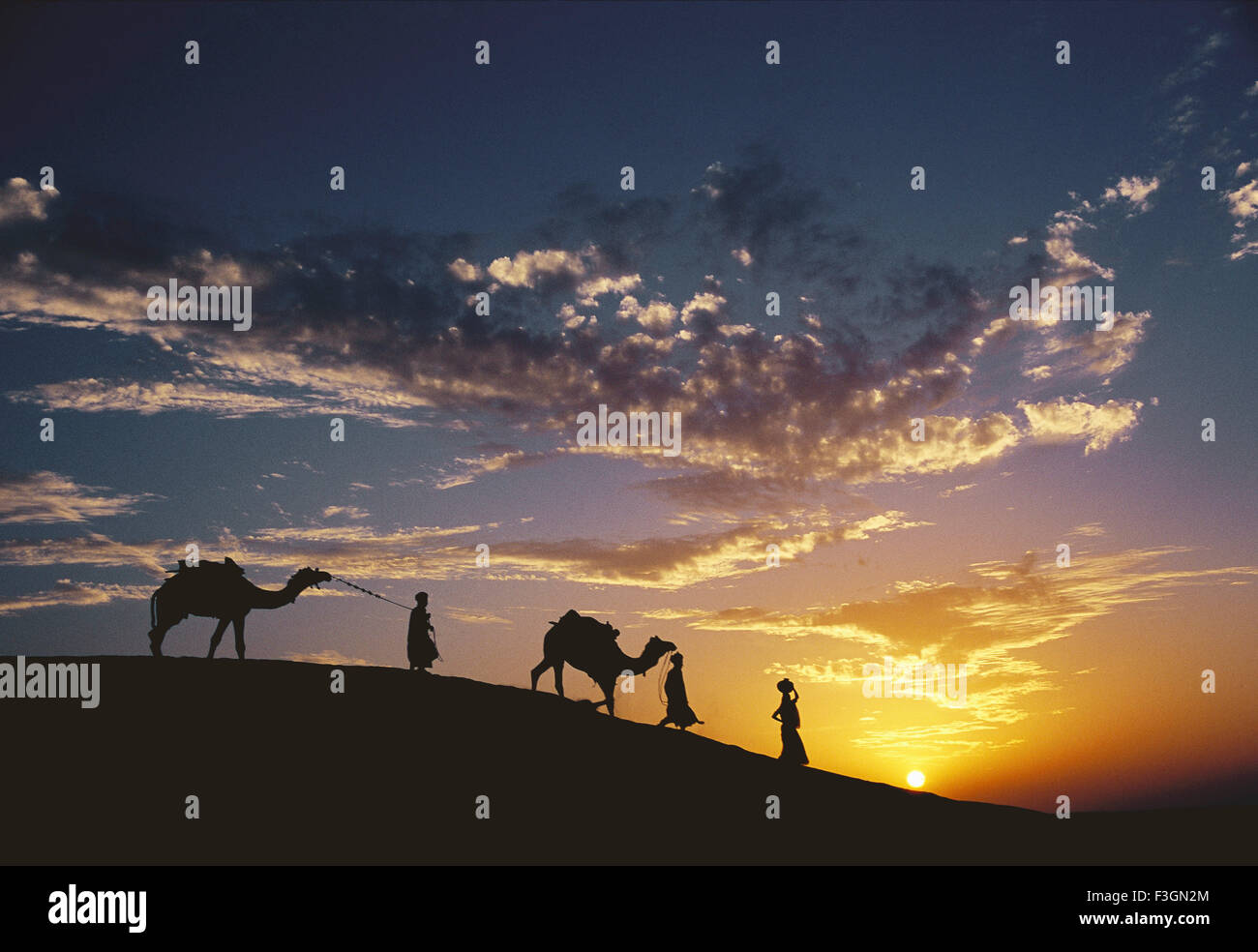 Gli uomini a piedi con i cammelli e le donne che trasportano acqua pentole vista serale del deserto Foto Stock