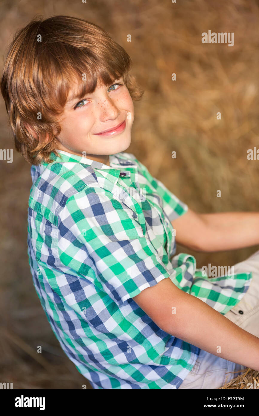 Giovani sorridenti ragazzo che indossa un plaid shirt e seduti sulle balle di fieno o paglia Foto Stock