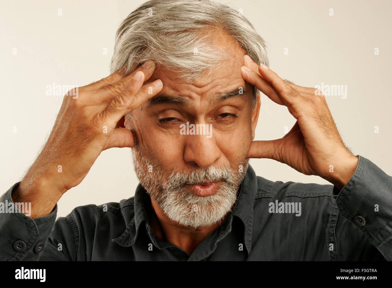 Indian vecchio uomo tardi anni cinquanta capelli grigi indossando maglietta blu che esprime grave cefalea premendo sulla fronte le dita delle mani irritato Foto Stock