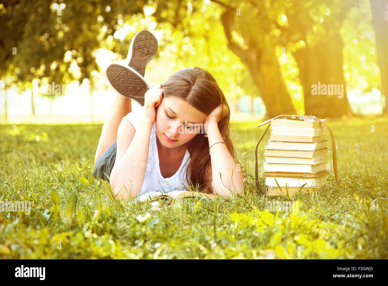 Bella giovane studente di college girl sdraiati sull'erba verde e la lettura di un libro presso il campus a caldo giorno. L'istruzione. Torna alla Foto Stock