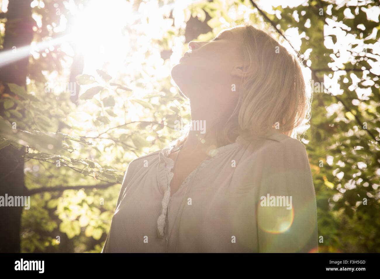 Donna matura in piedi nel flusso di luce nella foresta Foto Stock