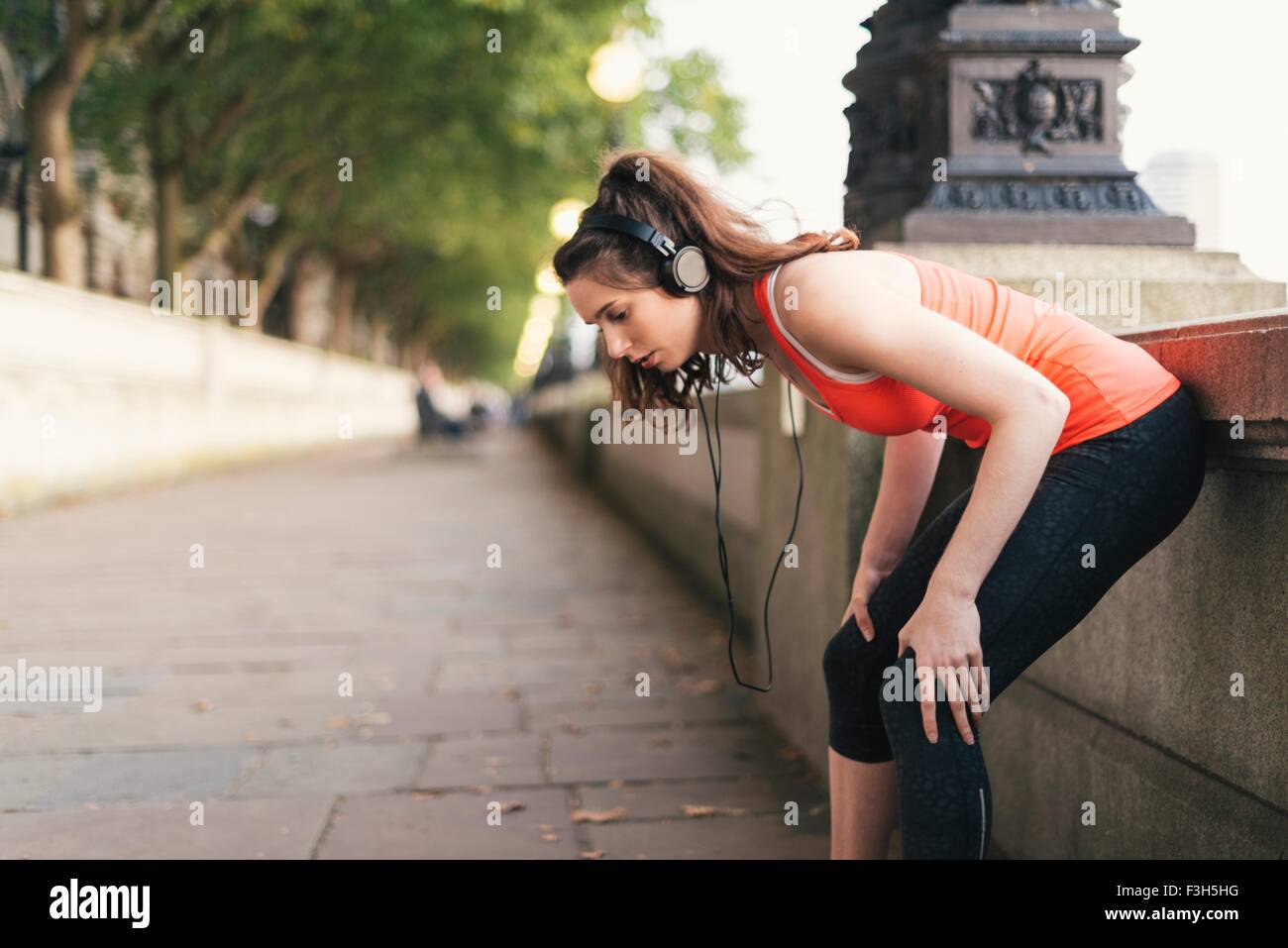 Giovani femmine runner indossa le cuffie prendendo una pausa su Riverside Foto Stock