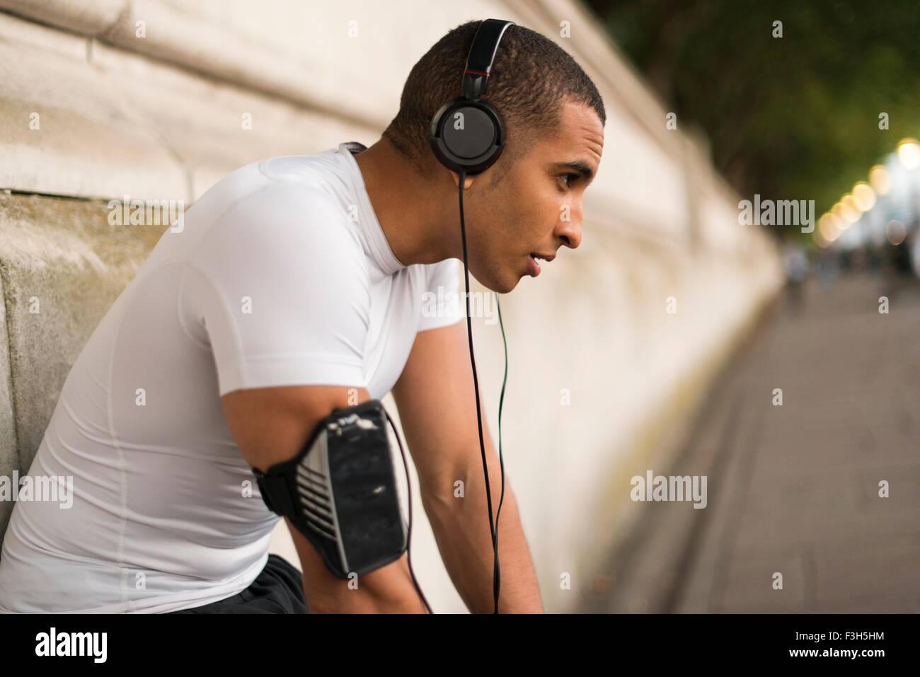 Esaurito maschio runner indossa le cuffie prendendo una pausa su Riverside Foto Stock