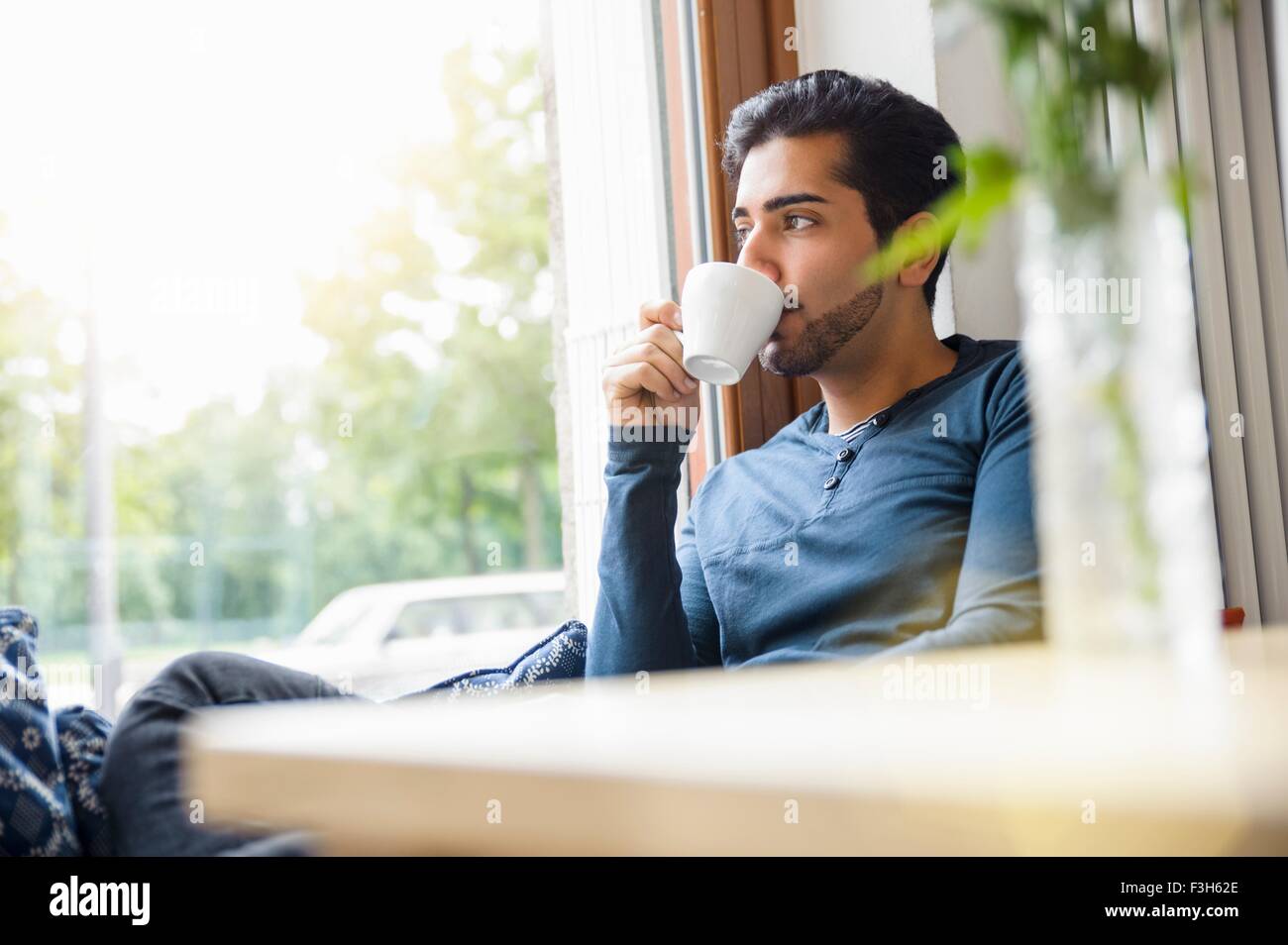 Giovane uomo seduto di fronte alla finestra di bere caffè, guardando lontano Foto Stock