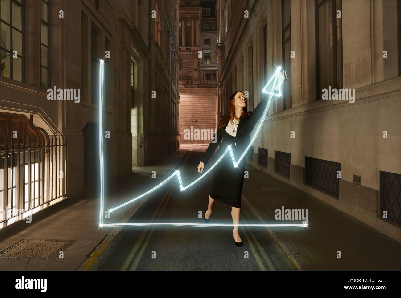 Imprenditrice pittura luce incandescente grafico con freccia in alto sul simbolo sulla via della città di notte Foto Stock