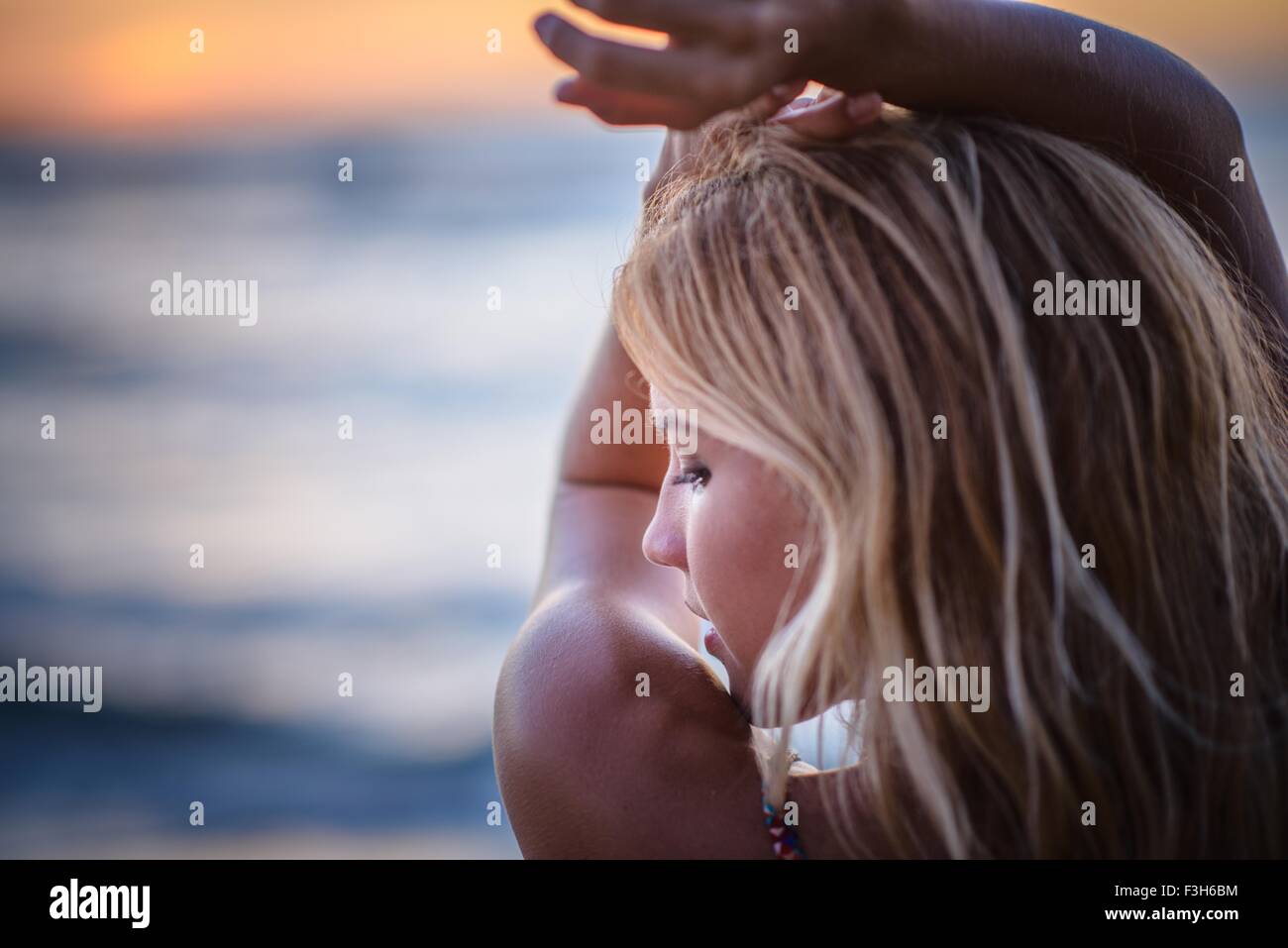 Giovane donna con le braccia sollevate sulla spiaggia al tramonto Foto Stock