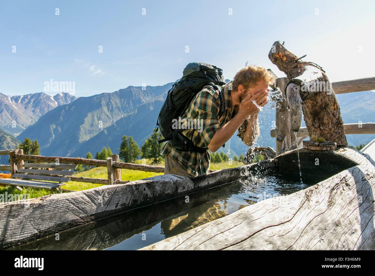 Giovane maschio escursionista faccia il lavaggio nel trogolo rustico, Certosa, Val Senales Alto Adige - Italia Foto Stock