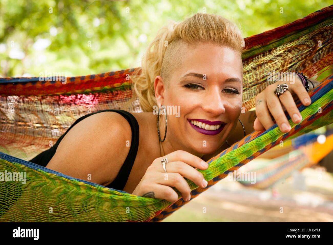 Ritratto di metà donna adulta con radere i capelli biondi giacente in giardino amaca Foto Stock