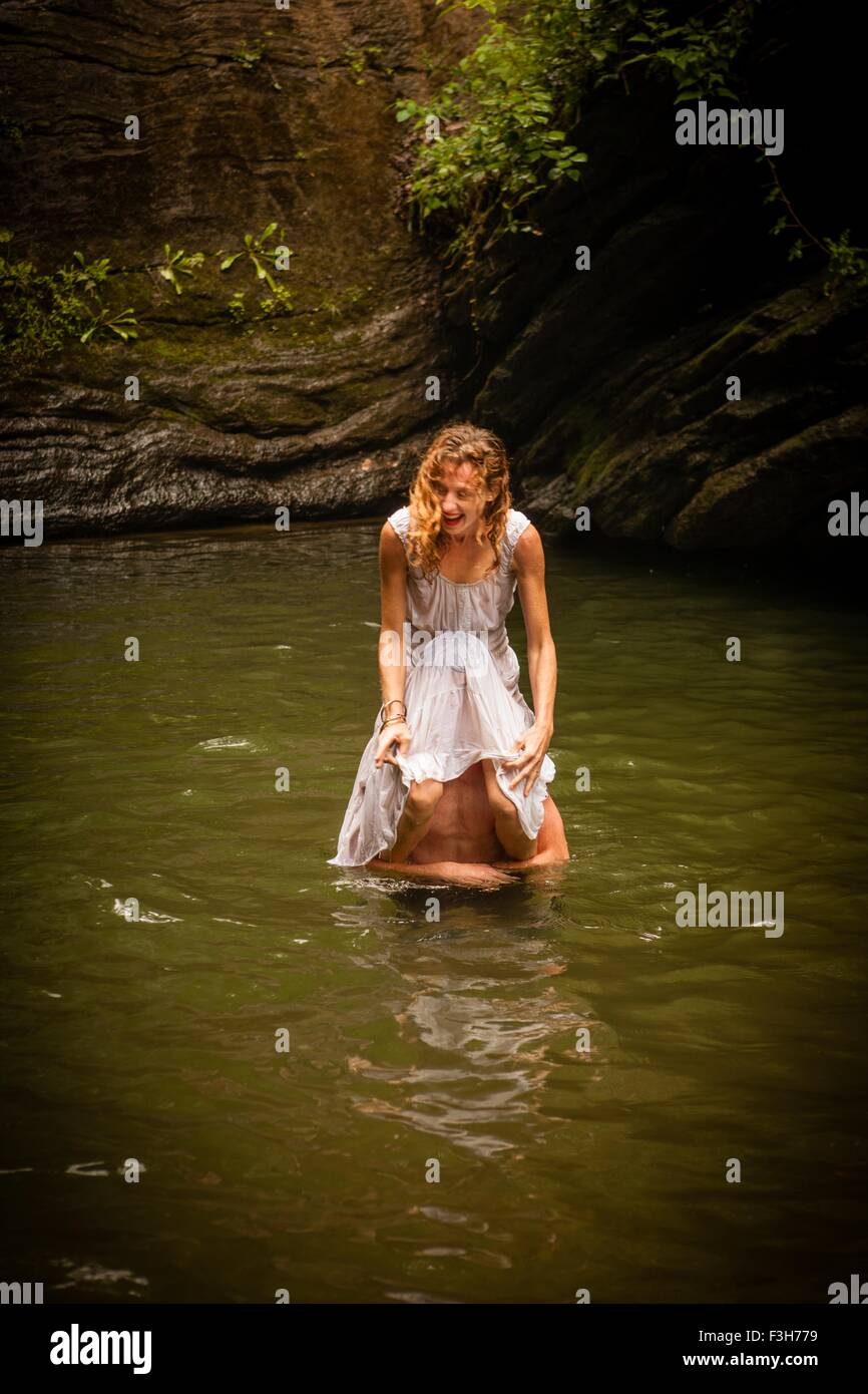 Metà donna adulta indossando abito bianco seduti sulle spalle dell uomo in acqua ridendo Foto Stock