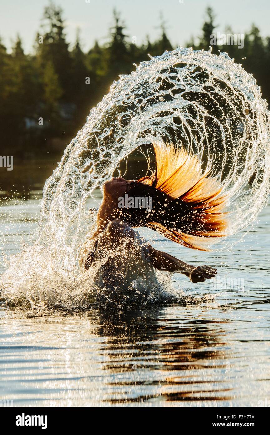 Vista laterale della giovane donna in acqua gettando i capelli bagnati bracci posteriore aperto Foto Stock