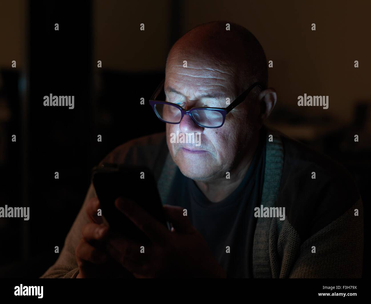 Uomo maturo utilizza lo smartphone durante la notte, viso illuminato Foto Stock