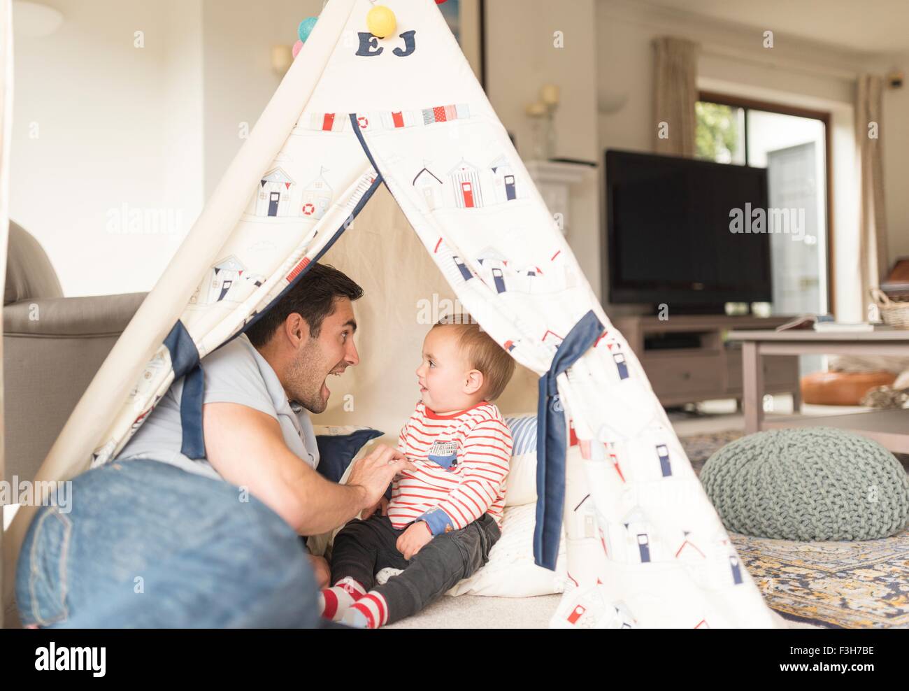 Padre e figlio giovane seduto in gioco tenda in interni, ridere insieme Foto Stock