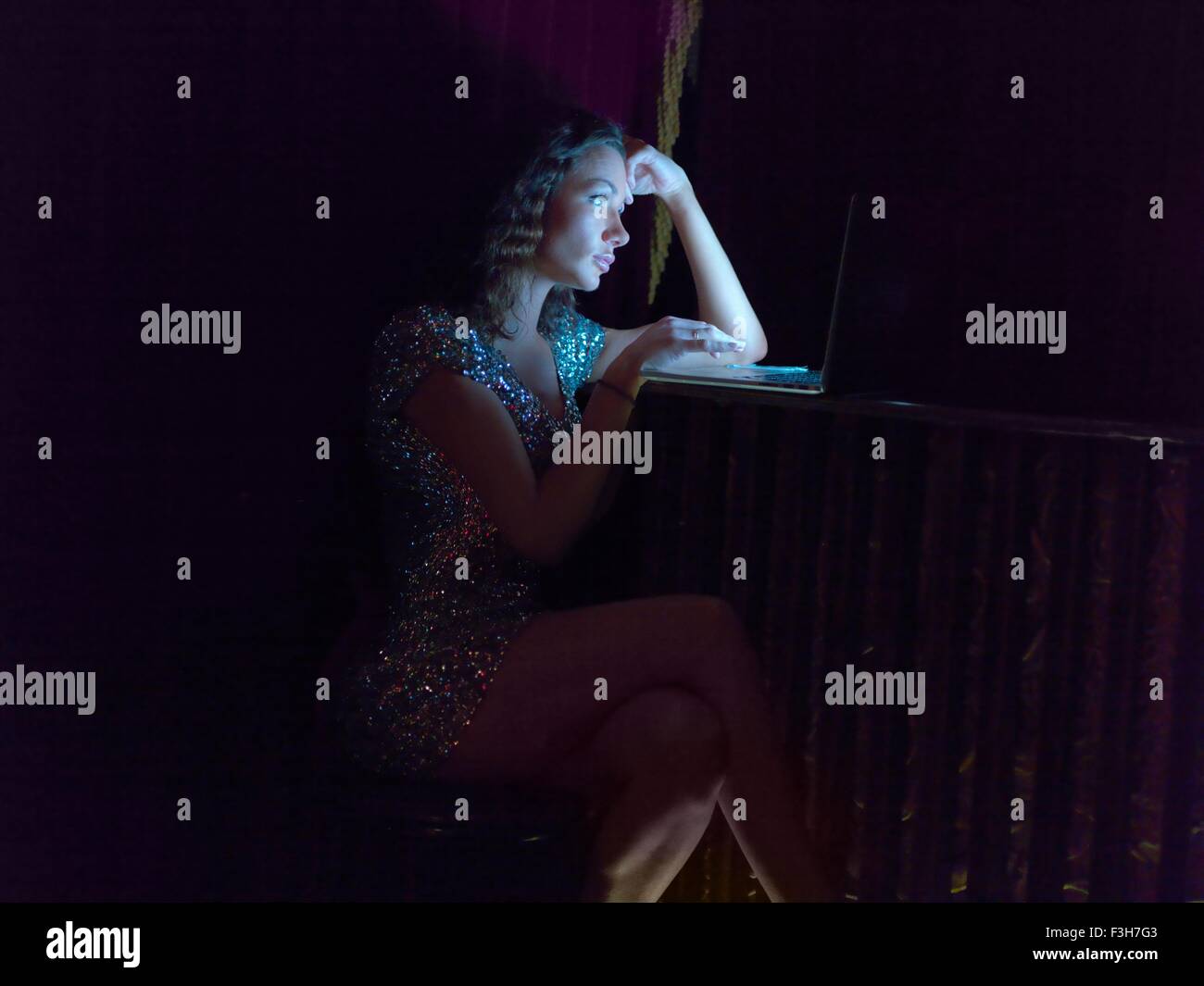 Metà donna adulta seduta nel bar la sera, utilizzando laptop Foto Stock