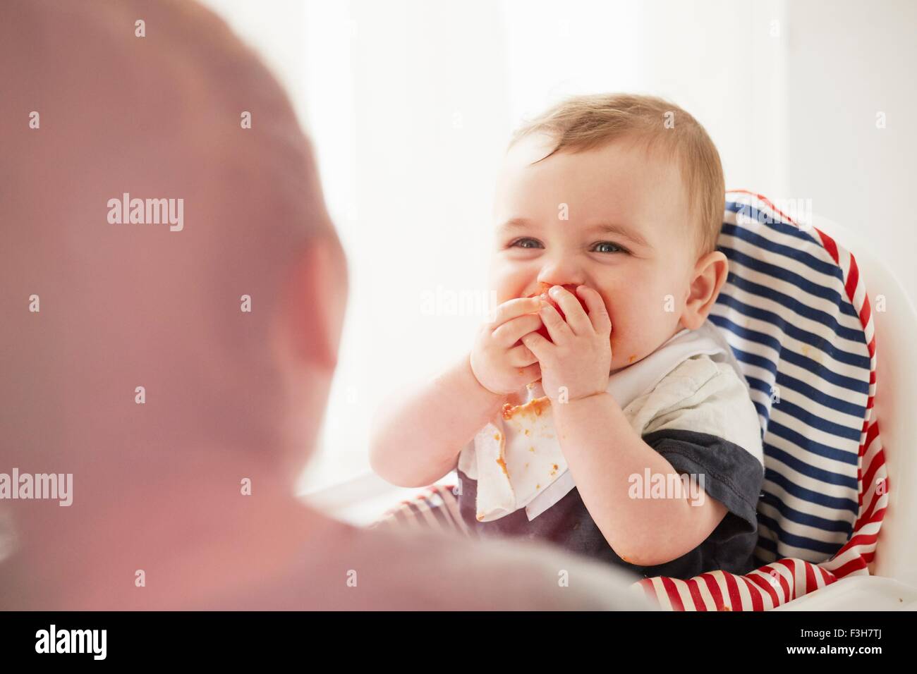 Baby boy alimentazione di se stesso nella Sedia bambino Foto Stock