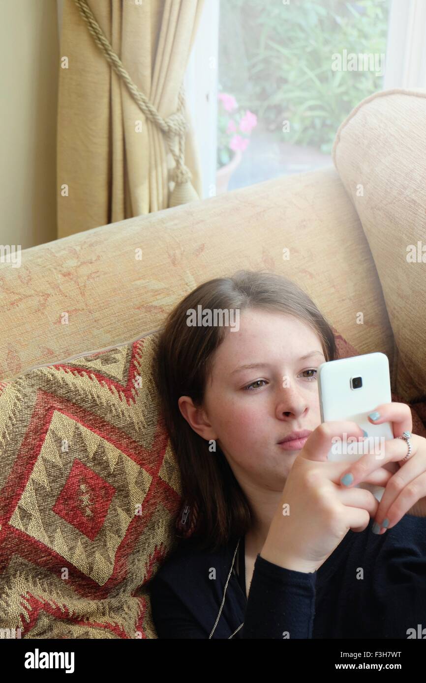 La testa e le spalle del giovane donna seduta sul divano la digitazione sullo smartphone Foto Stock