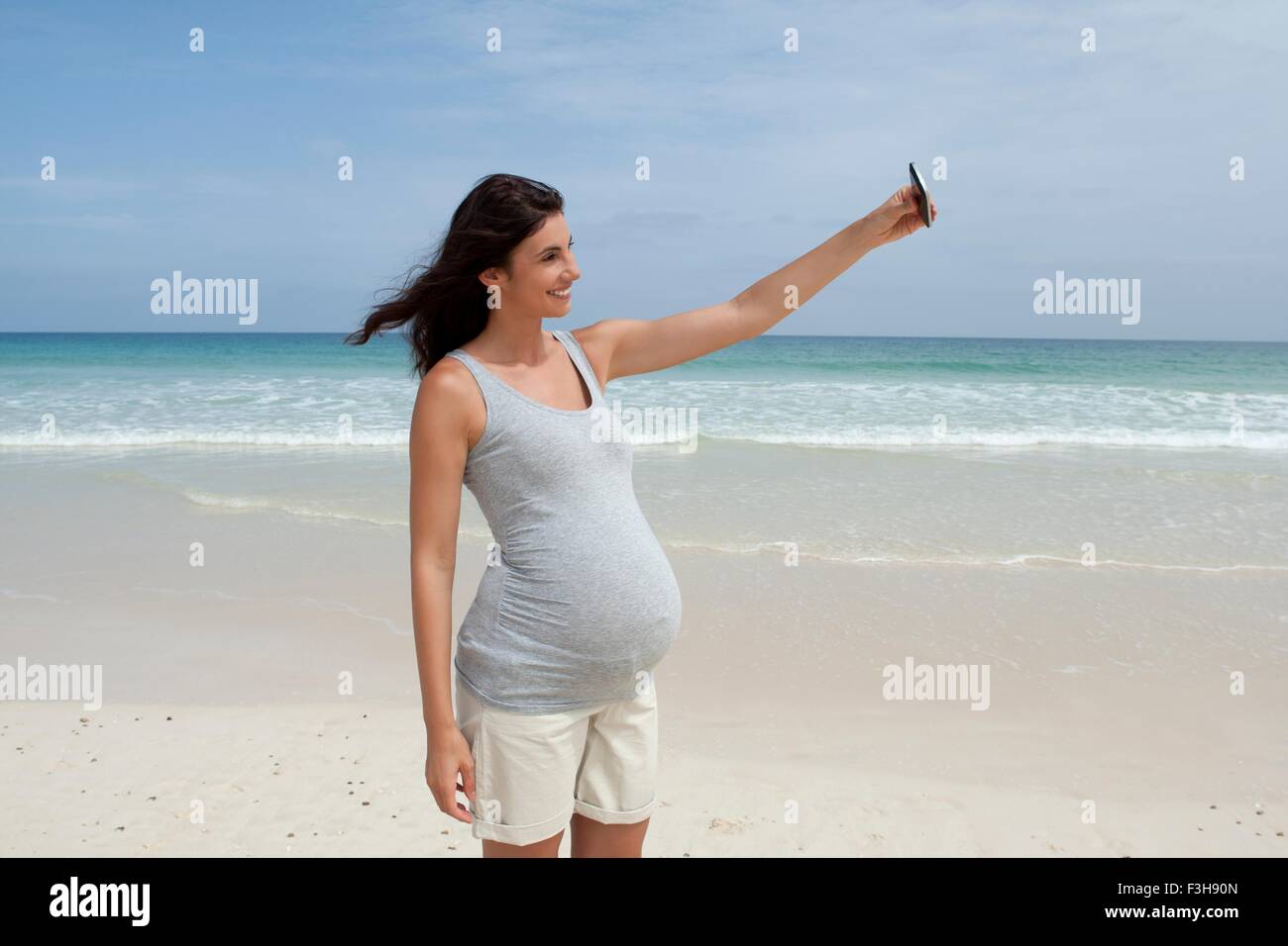 Gravidanza metà donna adulta prendendo selfie sullo smartphone in spiaggia, Capo Verde, Africa Foto Stock