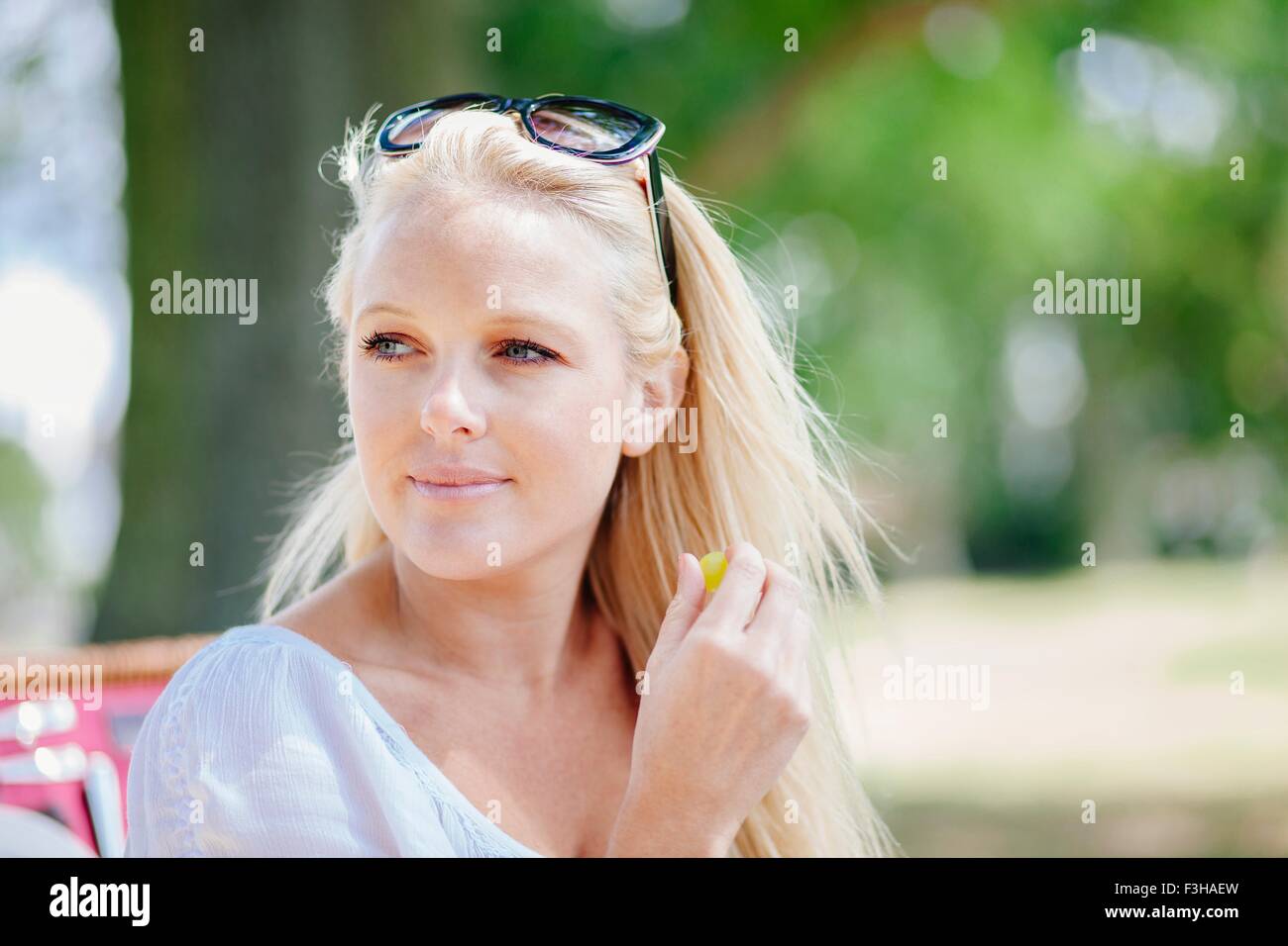 Ritratto di capelli lunghi giovane donna bionda con occhiali da sole sulla testa guardando lontano sorridente Foto Stock