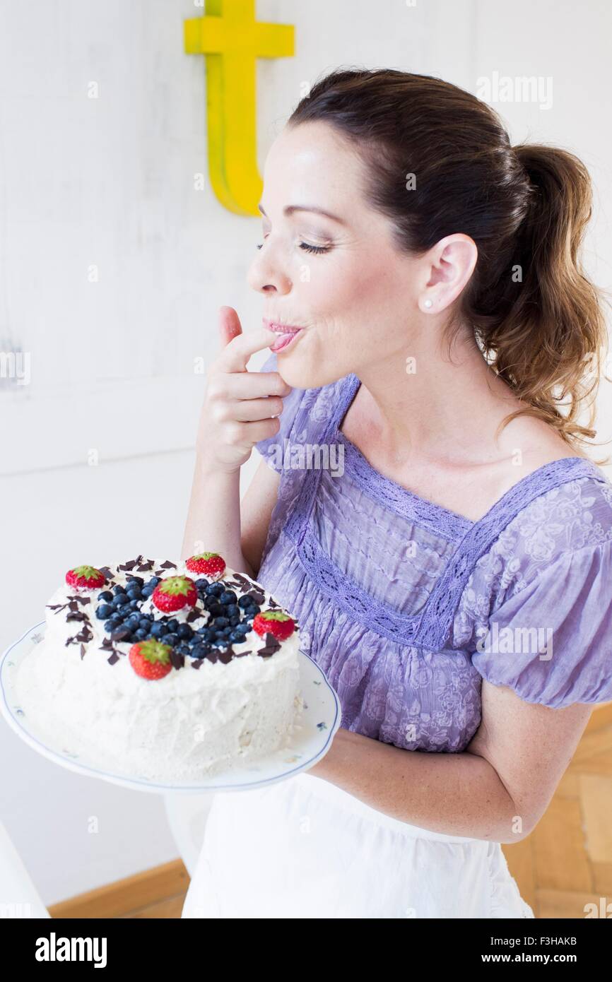 Donna matura azienda frutta coperta torta, leccarsi le dita gli occhi chiusi Foto Stock