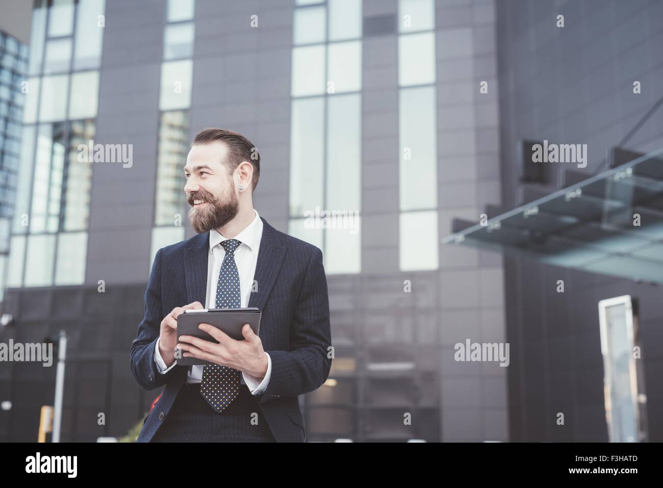 Elegante imprenditore barbuto con tavoletta digitale touchscreen fuori ufficio Foto Stock