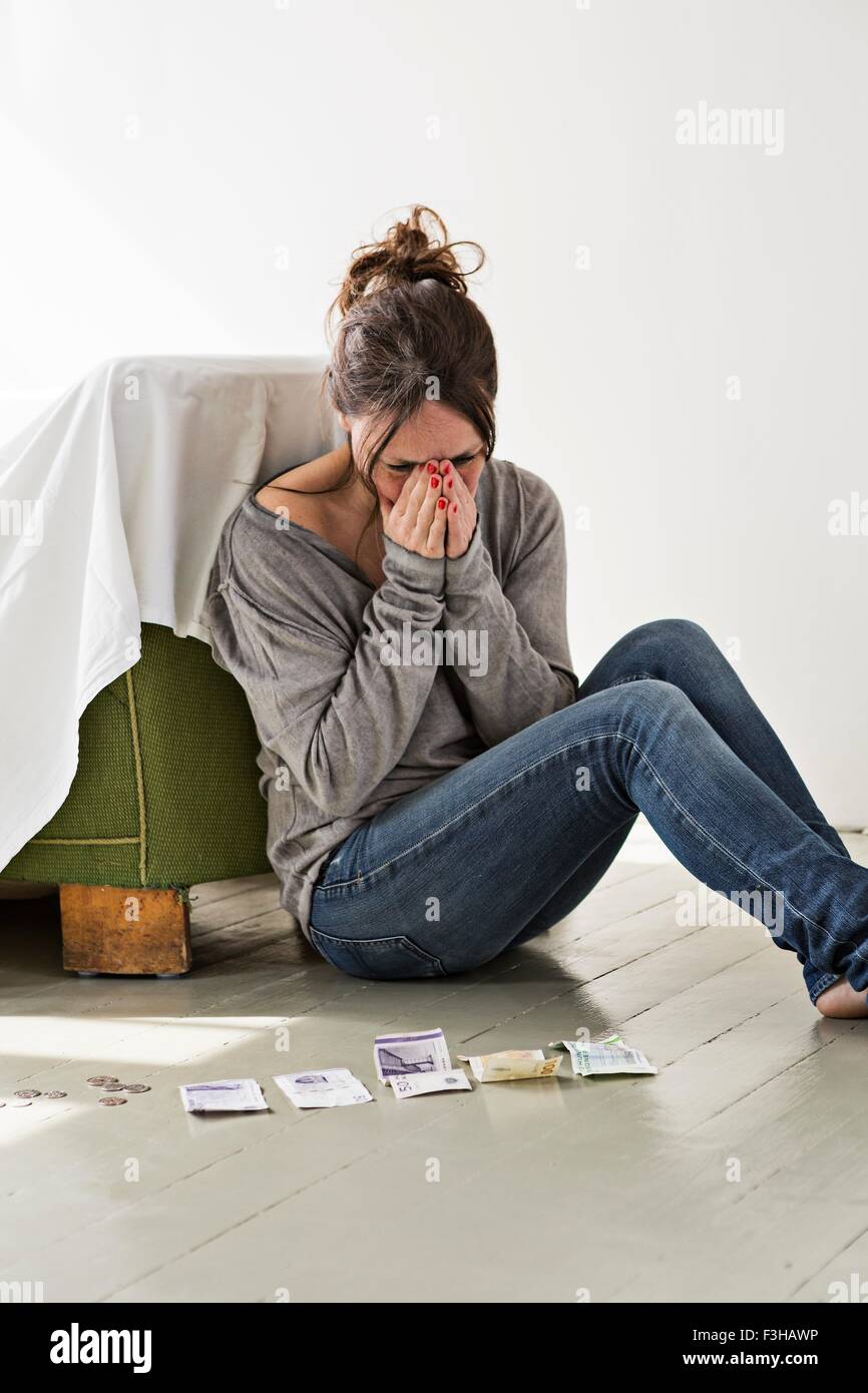 Donna matura seduti sul pavimento in casa, contando i soldi, distressed expression Foto Stock