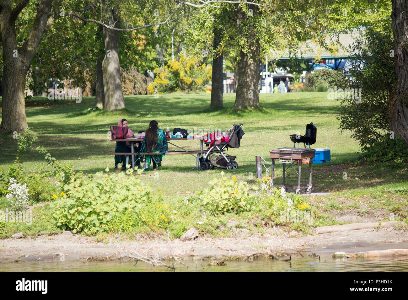 Due donne musulmane seduti ad un tavolo da picnic sull'isola centrale con il bambino passeggino rilassante in una giornata di sole. Foto Stock