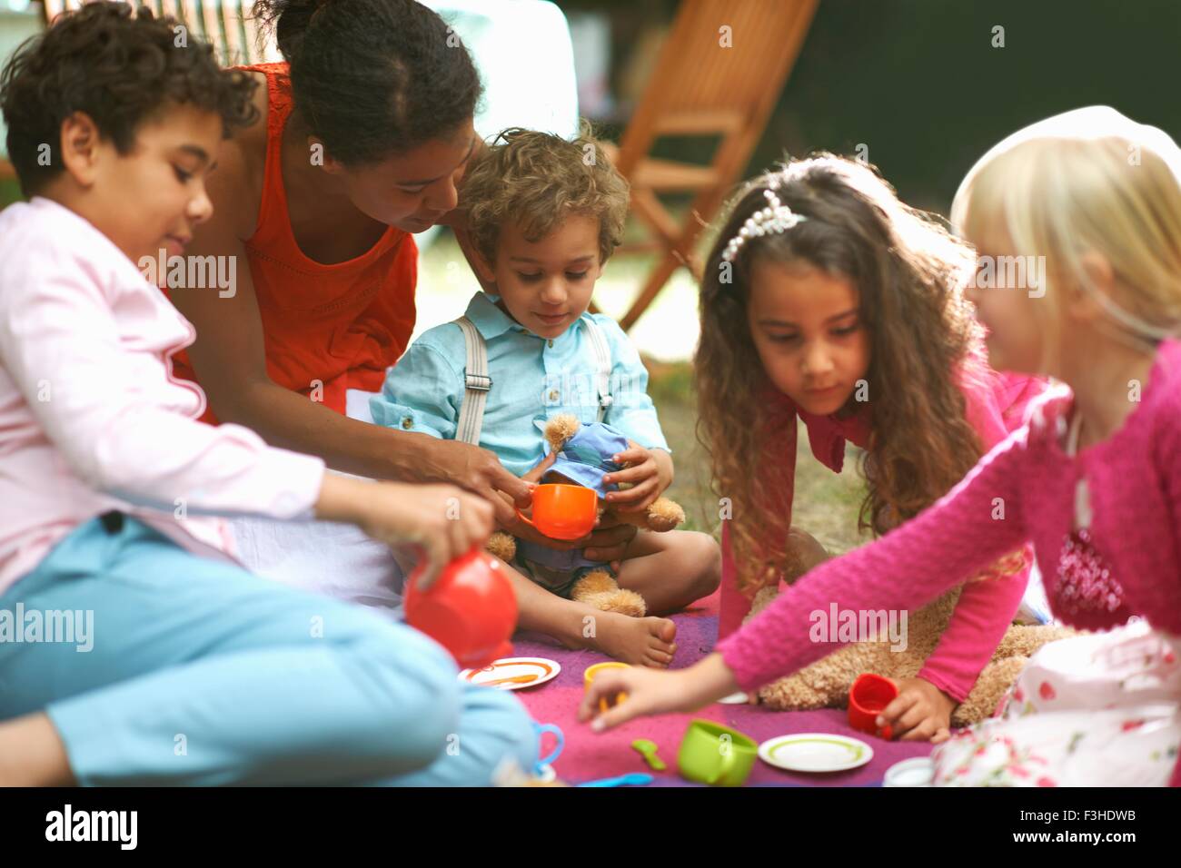 Madre e quattro bambini che giocano un pic-nic in giardino festa di compleanno Foto Stock
