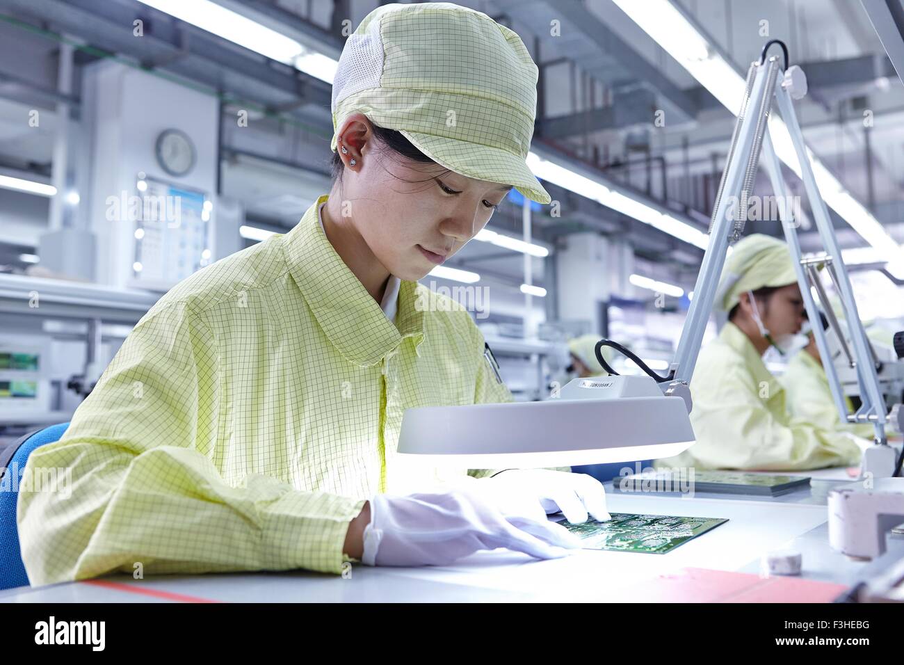Giovane donna una qualità di lavoro stazione di controllo di fabbrica di produzione flessibile di schede a circuito elettronico Foto Stock