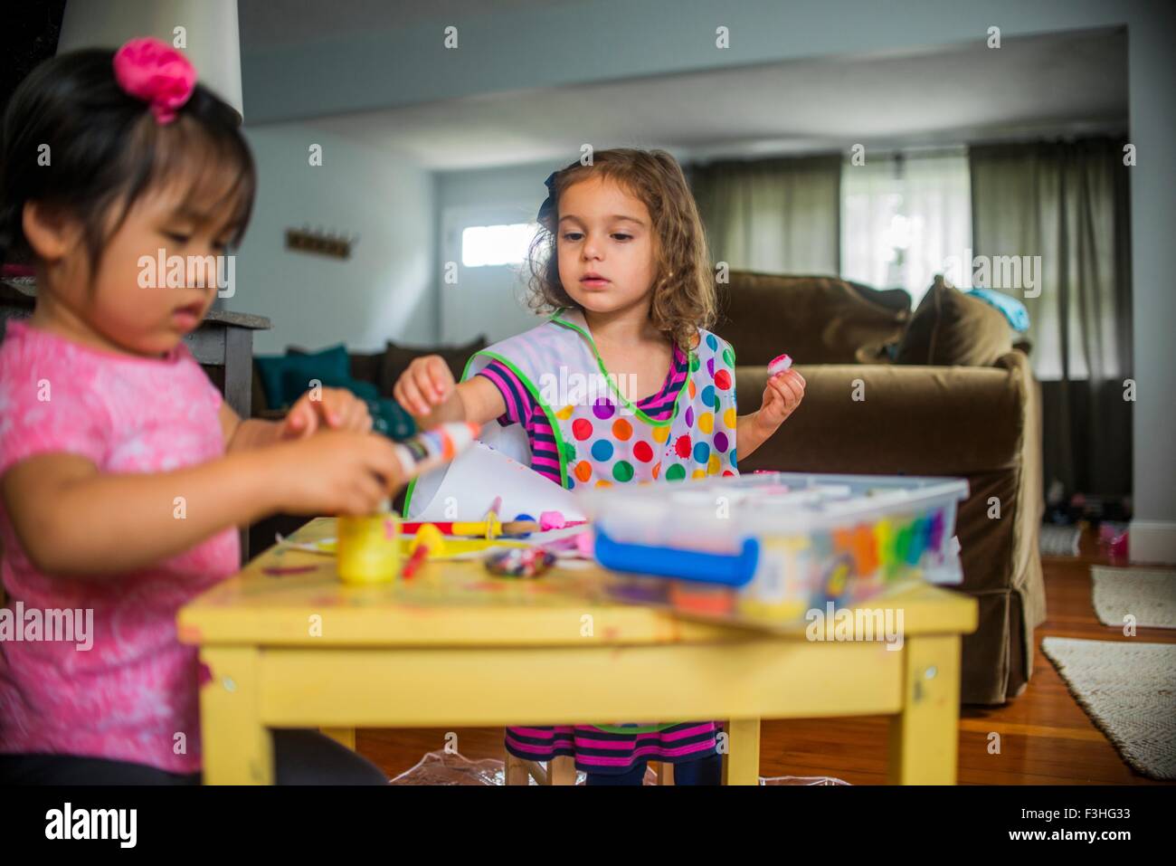 Due giovani ragazze seduta a tavola, fare arte, utilizzando una vernice Foto Stock